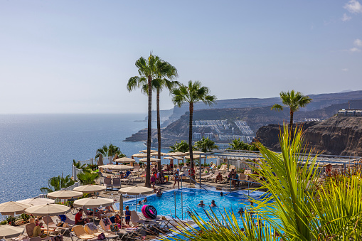 Gran Canaria. Spain. 07.16.2023. Beautiful view of people bathing in hotel outdoor pool on backdrop of Atlantic Ocean.