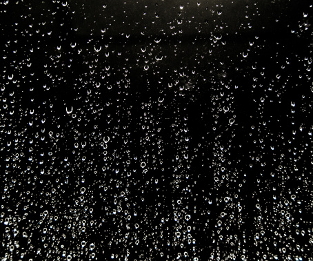 Heavy rain drops on a window with black background.
