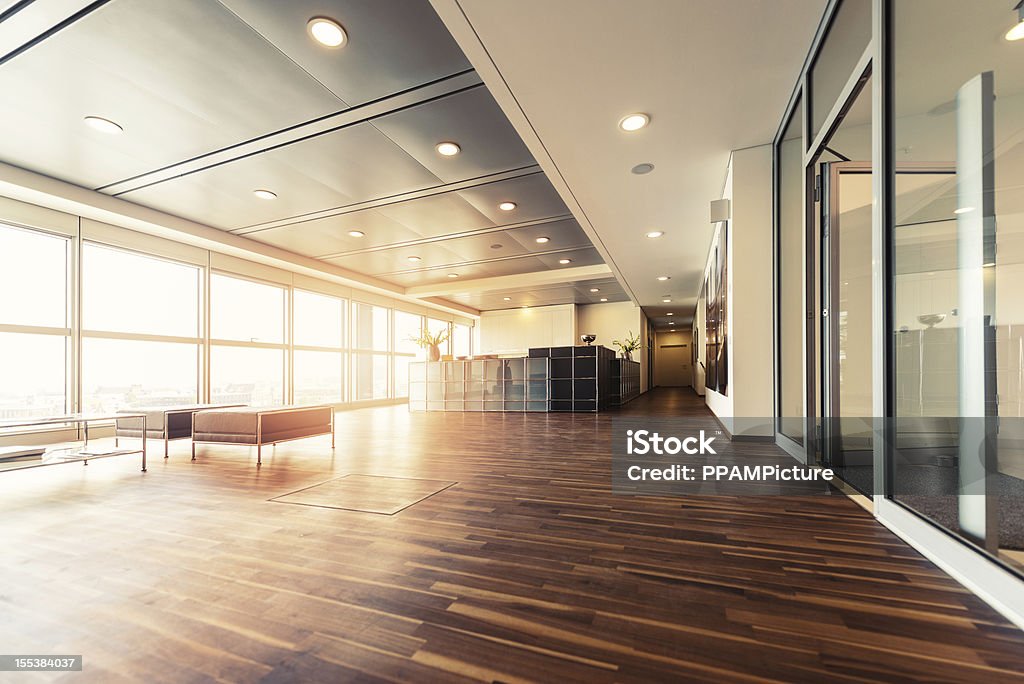 Office reception with wood floors and window wall A large open plan office space with a wooden floor and decorative ceiling.  Full height windows run along the full length of the office space. Office Stock Photo