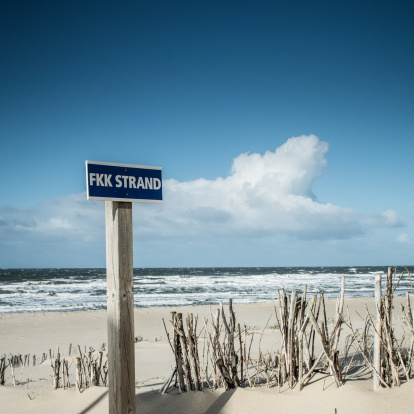 A nude beach sign at a nudist area on the the beach of Kampen (Sylt - Germany) near by the famous place Buhne 16. On a very windy and  sunny day. Copy space on the blue sky in the background.