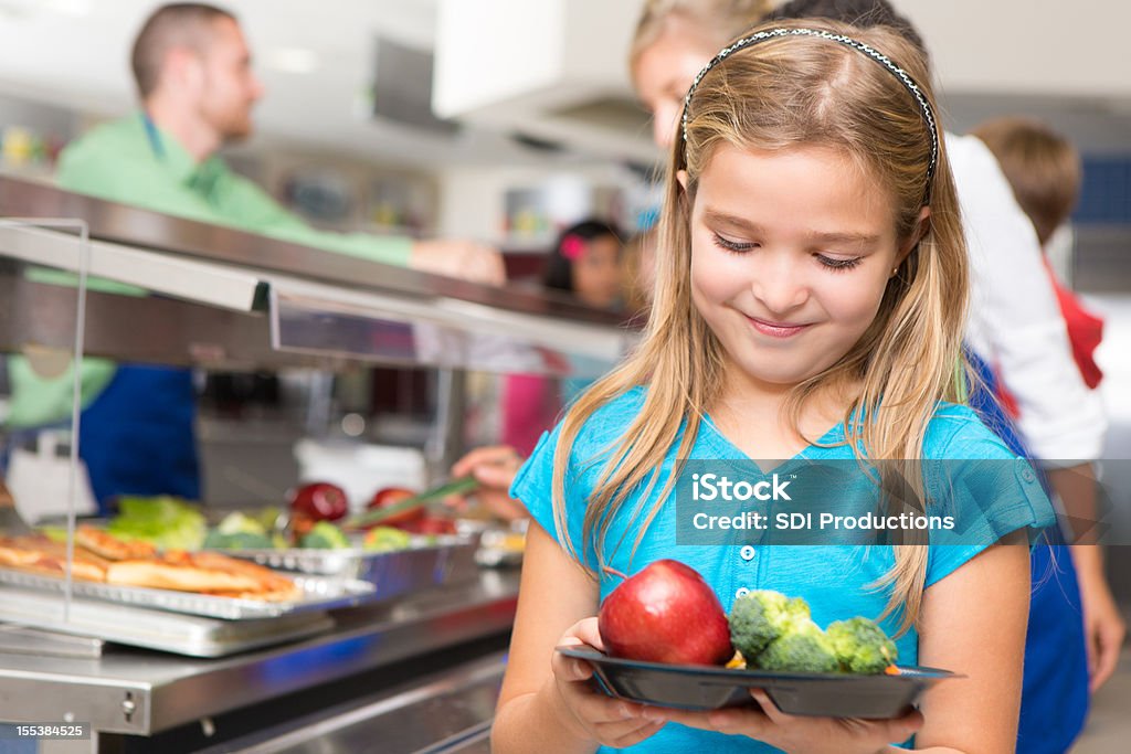Счастливый Маленькая девочка, делая здоровый выбор в школьной столовой - Стоковые фото Школьный обед роялти-фри