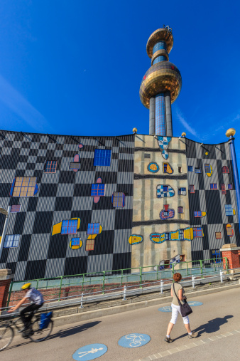 People on the bike and pedestrian way that passes close to the incinerator of Spittelau (Müllverbrennungsanlage Spittelau), a thermal waste treatment plant of the city of Vienna. Completed in 1971 and redesigned externally by Austrian artist Friedensreich Hundertwasser, today stands out among the surrounding industrial buildings, and it has become a tourist attraction.