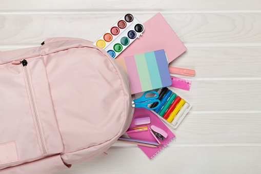 Pink school backpack with stationery on wooden background, top view