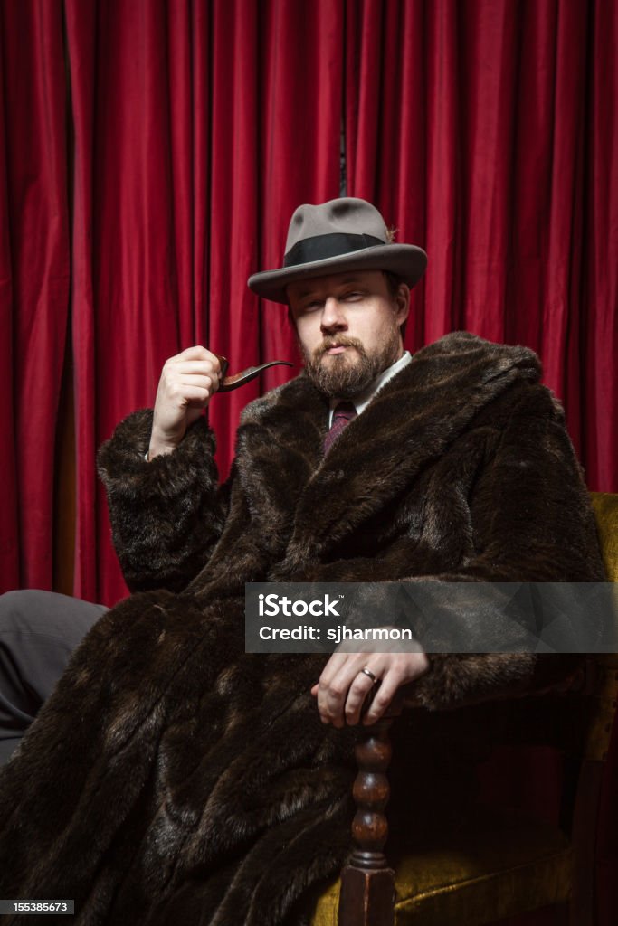 Seated Bearded Man Wearing Fedora, Fur Coat, Holding Pipe  Sitting Stock Photo