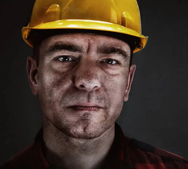 Portrait of a miner with yellow helmet against dark background.