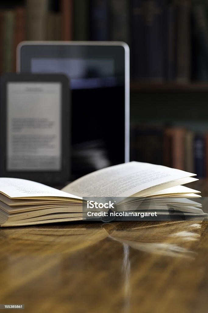 Books and E-readers Old books and digital readers in the background with a book in the foreground.  Very shallow focus on front edge of book. E-Reader Stock Photo