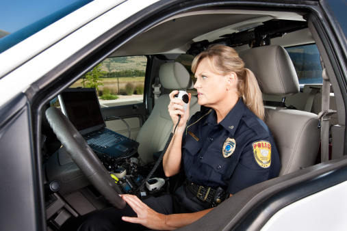 Action shot of a mature woman law enforcement officer sitting in her patrol vehicle and talking on a corded hand held radio, communicating with dispatch during a traffic stop.