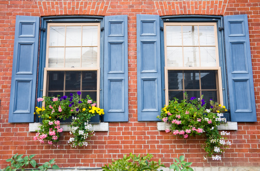 A red brick home with blue shutters around the windows and with blooming summer flower boxes.