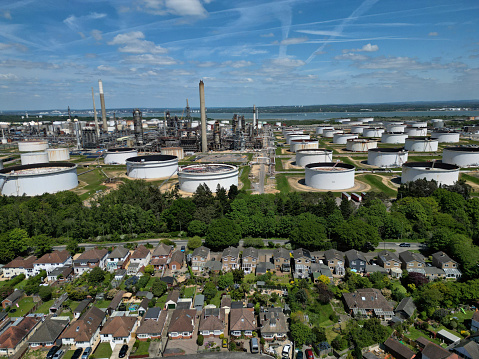 Aerial shot of Fawley village and residential housing in front of the biggest oil refinery and petrochemical complex in the UK. Oil refinery is based in Fawley, Hampshire. Hundreds of oil storage tanks. At Fawley refinery they produce petrol, diesel, kerosene, heating oil, propane and other chemical products.