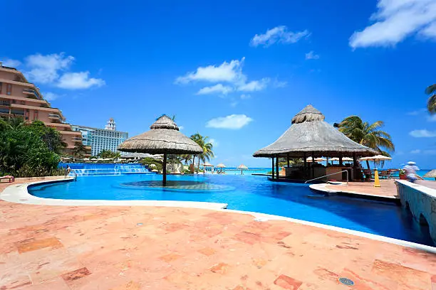 Cancun area luxury hotel pool with palm trees, hut umbrellas and tiki bar