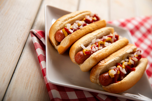 This is a photograph of three hot dogs on a white plate on a white wooden picnic bench. This is a great image for a Fourth of July picnic.