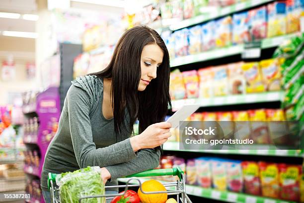 A Woman Refers To Her Shopping List While Pushing A Cart Stock Photo - Download Image Now