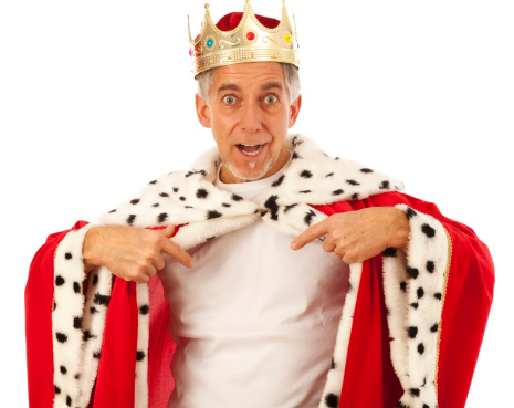 senior man wearing a king's robe and crown, pointing at his white t-shirt