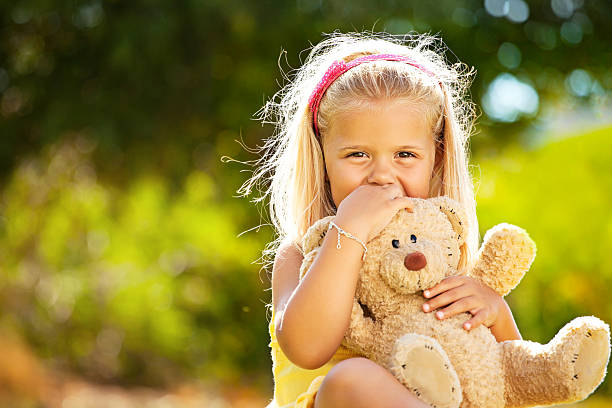 Beautiful little girl sitting outdoors holding a teddy bear.