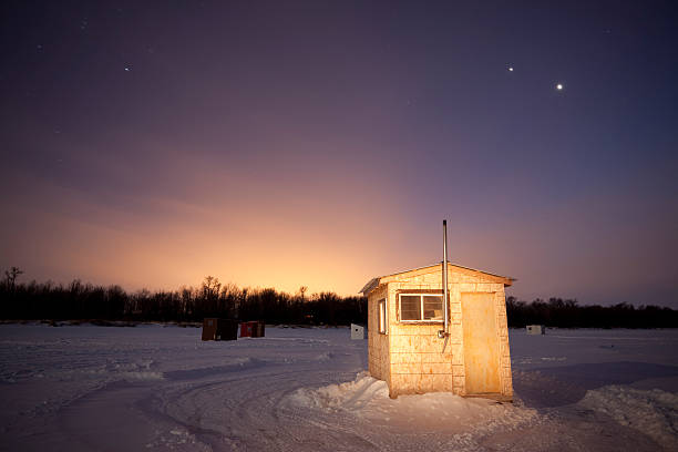 Small ice fishing huts at sunset Ice fishing hut on the frozen Red River, 40 mins out side of Winnipeg. I used a flash light to illuminate the front of the hut. Image taken from a tripod. City of Winnipeg lights glowing 40 mins drive away. ice fishing stock pictures, royalty-free photos & images