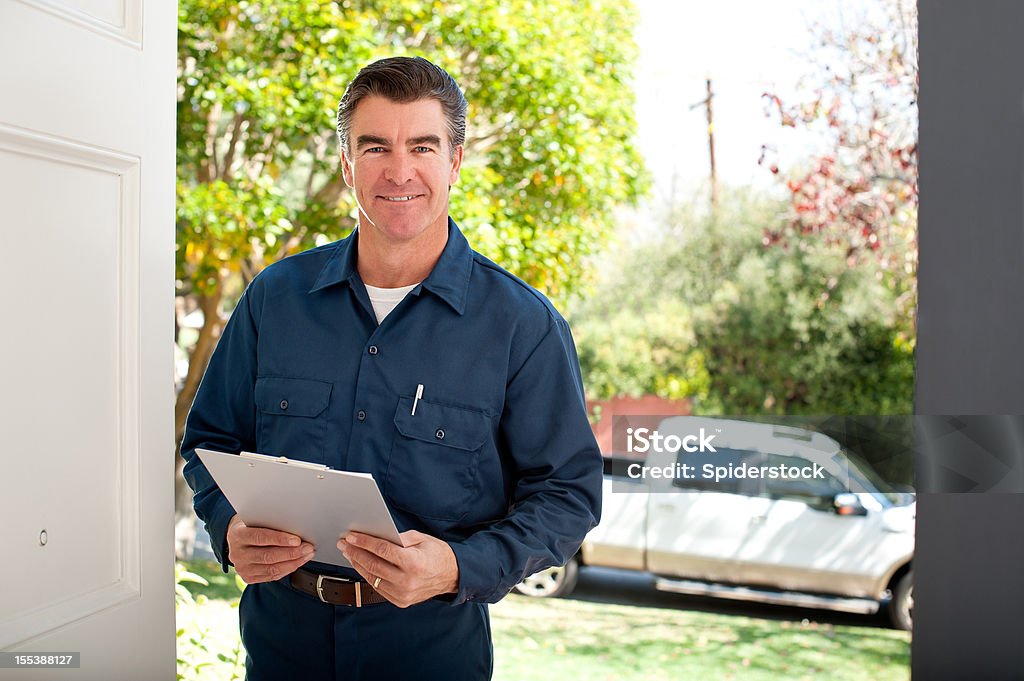 Repairman In Uniform Good looking repairman in uniform holding a clipboard with his pick up truck behind him. Building Contractor Stock Photo