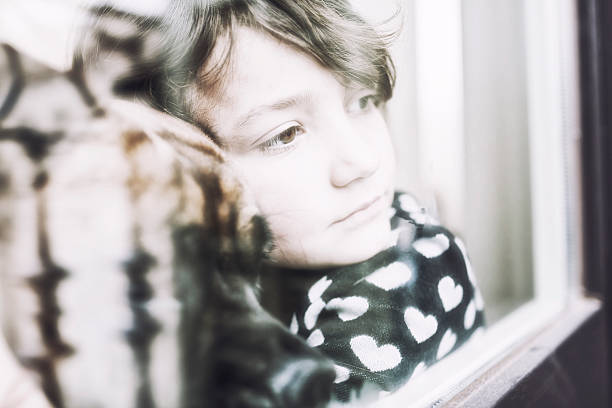 istock Pensive child looking through a window with her dog 155388426