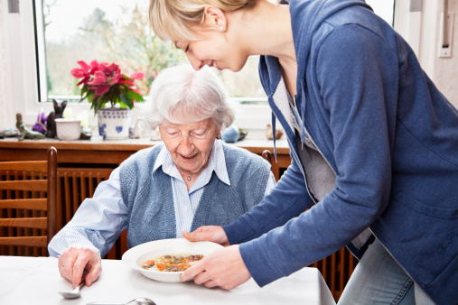 senior woman getting soup served by young home caregiver