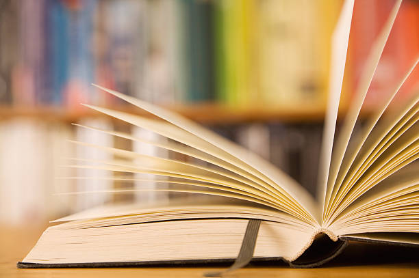 An open book with a leather bookmark Sideview of an open book lying in front of bookshelf with books sorted in spectrum. rows of books stock pictures, royalty-free photos & images