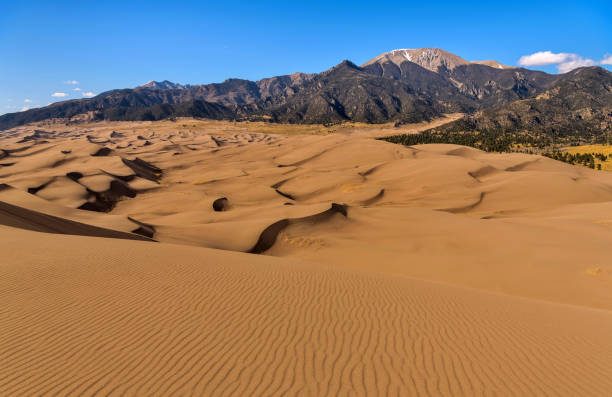 istock Sand Waves and Ripples - A panoramic Spring evening view of rolling sand dune waves and pristine sand ripples at base of Mt. Herard. Great Sand Dunes National Park, Colorado, USA. 1553893895