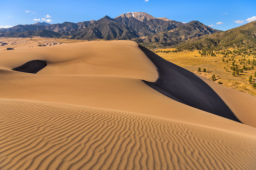 A panoramic overview of big pristine rolling sand dunes at base of Mt. Herard on a sunny but windy Spring evening. Great Sand Dunes National Park, Colorado, USA.