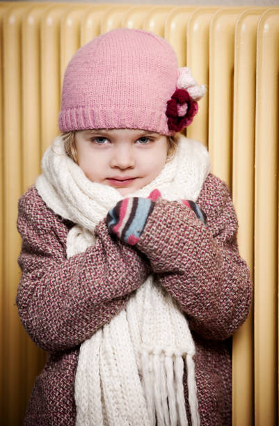 Girl in winter cloth in front of old radiator. Concept for energy crisis.