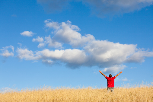 A man with his arms outstretched in a beautiful prairie scene. Horizontal colour image. Back view. Unrecognizable person. Caucasian. Additional themes include praying, meditation, praise and worship, Christianity, hope, freedom, salvation, faith, Christianity, religious, one man, male, alone, spirituality, and balance. 
