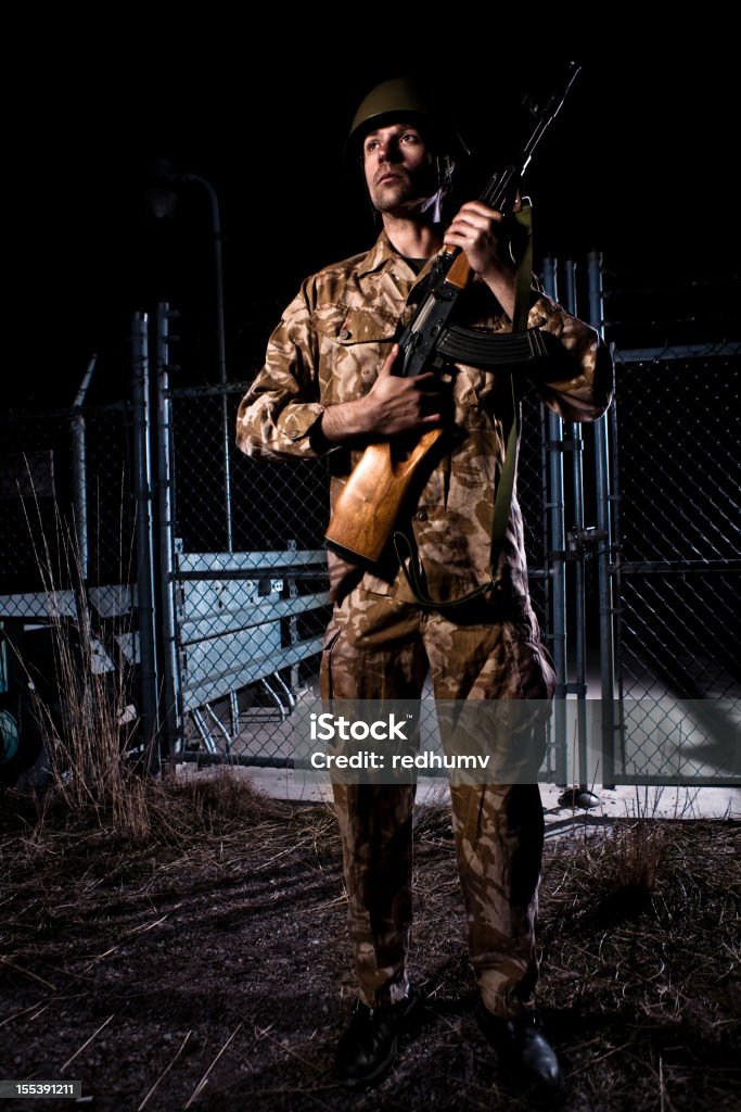 Checkpoint Soldier A stock photo of a young military soldier guarding a checkpoint or fence at night with a high powered assault rifle and hard hat helmet dressed in camo fatigues.http://www.bellaorastudios.com/banners/new01.jpg 20-29 Years Stock Photo