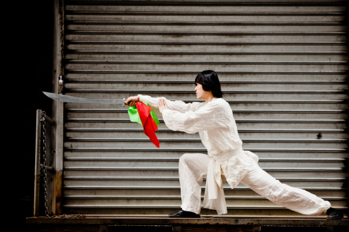 A kung fu warrior dressed all in white and practicing with the traditional sword (Kwan Do) of Kung Fu in an alley of New York City