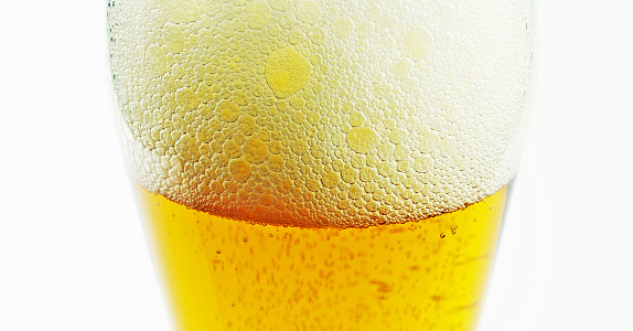 The foamng head on a glass of beer with a white background.