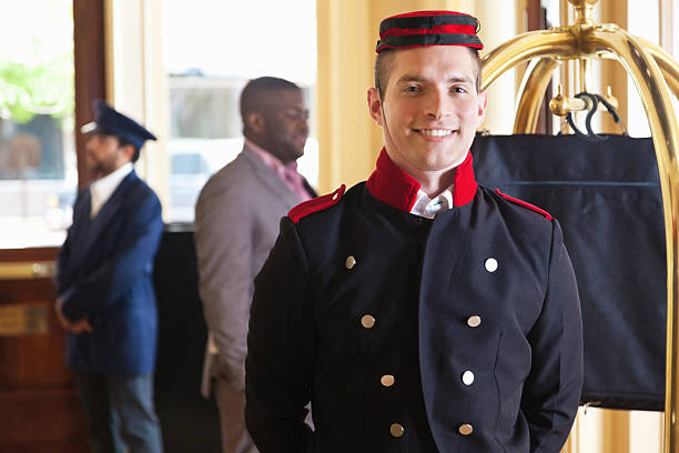 Bellhop standing in hotel lobby with guest's luggage on cart Bellhop standing in hotel lobby with guest's luggage on cart.  bellhop photos stock pictures, royalty-free photos & images