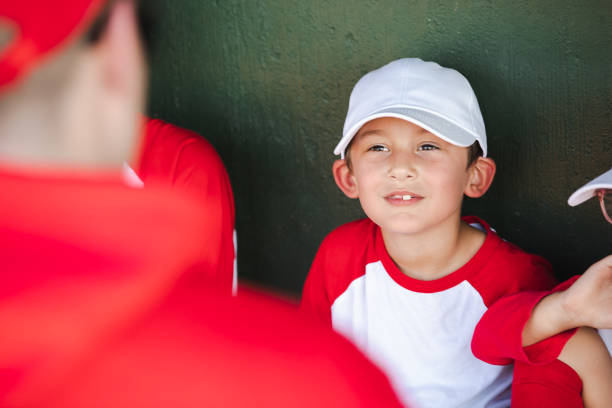 かわいい男の子がリトルリーグの野球の試合中にコーチと話しながらダッグアウトに座る - dugout baseball bench bat ストックフォトと画像
