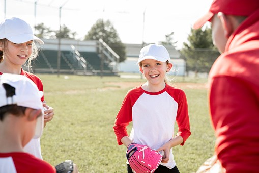 Cute little girl plays baseball with her friends on community little league field