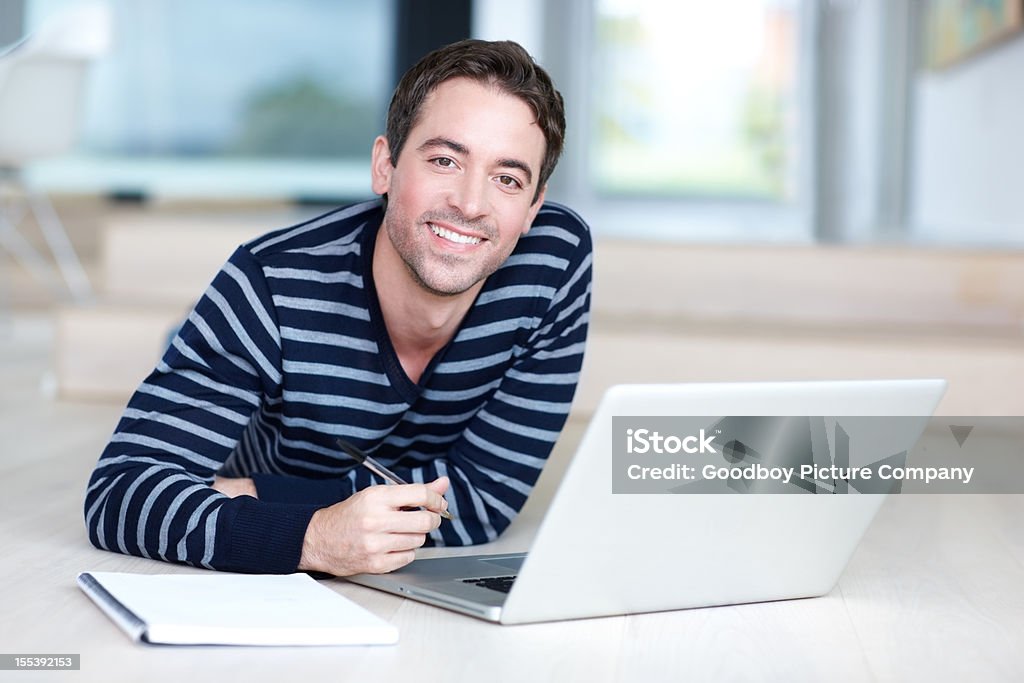 Young man with laptop on floor, smiling at camera  Adult Stock Photo