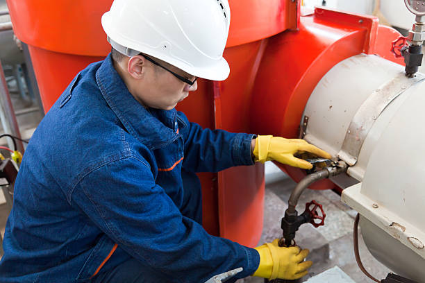 A worker wearing a hard hat collecting an oil sample 