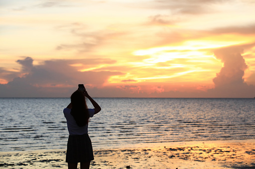 silhouette young women use mobile phones to shoot beautiful sunset sky over the sea, travel outdoor concept