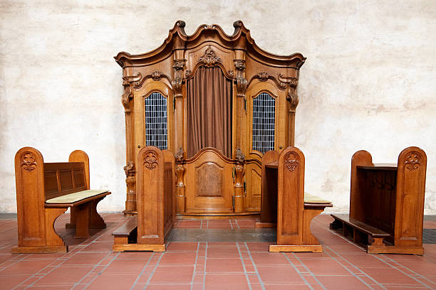 A vintage wooden confessional booth with curtains in a church interior, featuring a decorative terrazzo floor pattern.