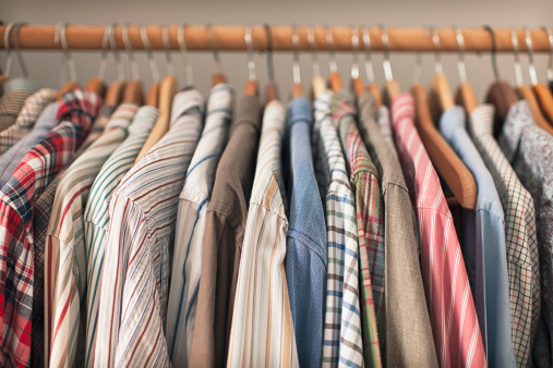 A variety of shirts hanging on a wooden clothes rack.
