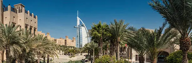 The iconic futuristic sails of the luxury Burj Al Arab hotel towering over the traditional wind towers and tranquil palm fringed oasis of the Madinat Jumeirah on the coast of Dubai, United Arab Emirates. ProPhoto RGB profile for maximum color fidelity and gamut.