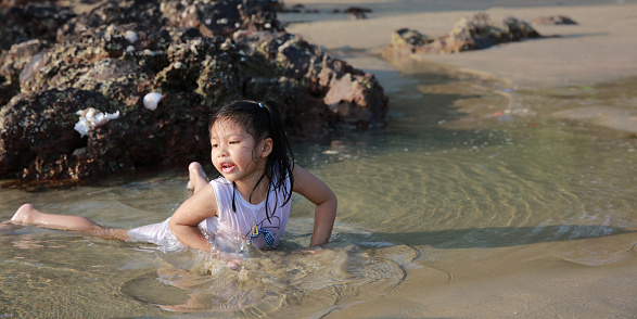 Happy and Funny girl lying down on the beach and playing in the sea on summer vacation