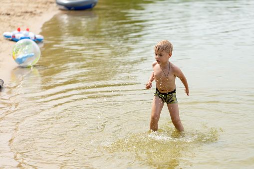 A little boy frolics in the water on the shore of a pond