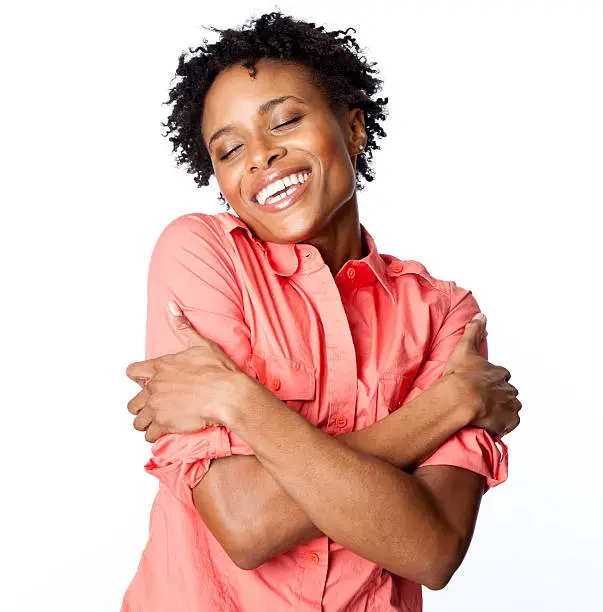 Happy curly-haired woman hugging herself - on white background