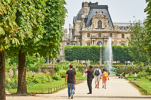 Paris, France - July 10, 2023: Pedestrians in the Tuileries Garden in Paris. In the background part of the Louvre.
