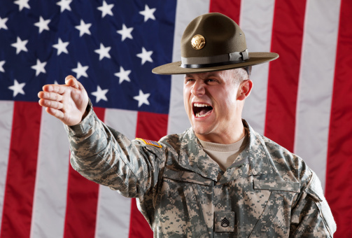 U S Army Drill Sergeant in Army Camouflage Uniform and hat against USA flag.