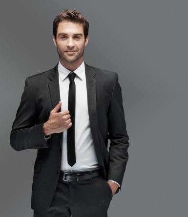 Young man in smart suit standing confidently next to copyspace, isolated on grey