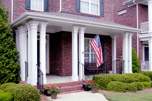 Detail of a cottage-style front porch with an American Flag hanging from the front column.