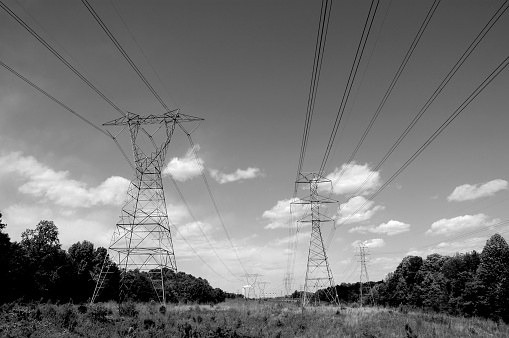 Wide angle, black and white photo of high-transmission power lines feeding from coal-powered, steam plant in background.