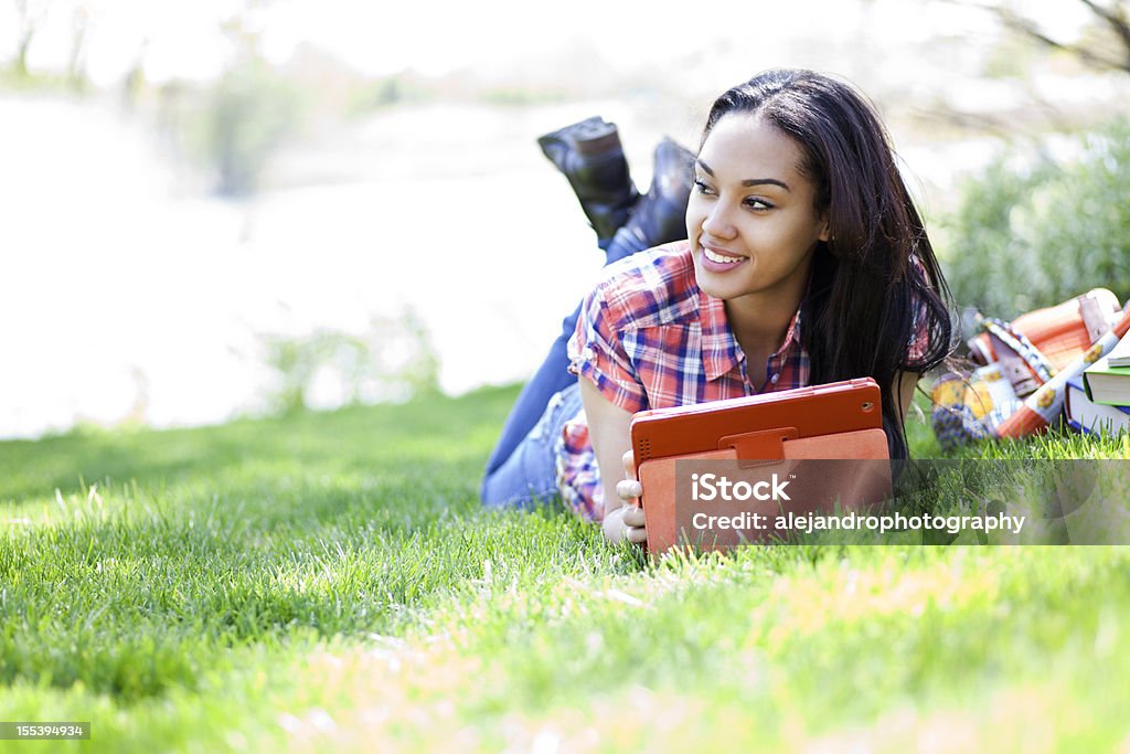 Student using digital tablet Beautiful mixed race young student laying down in a field using an E-reader or digital tablet Summer Stock Photo