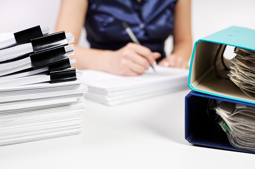 A stack of papers with Binder Clips against the background of an office worker working with documents