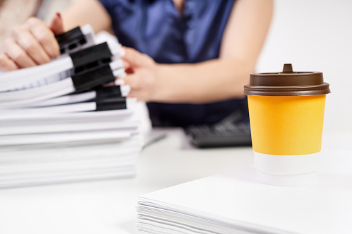 A cup of coffee on the background of an office worker sorts out a stack of papers fastened with Binder Clips